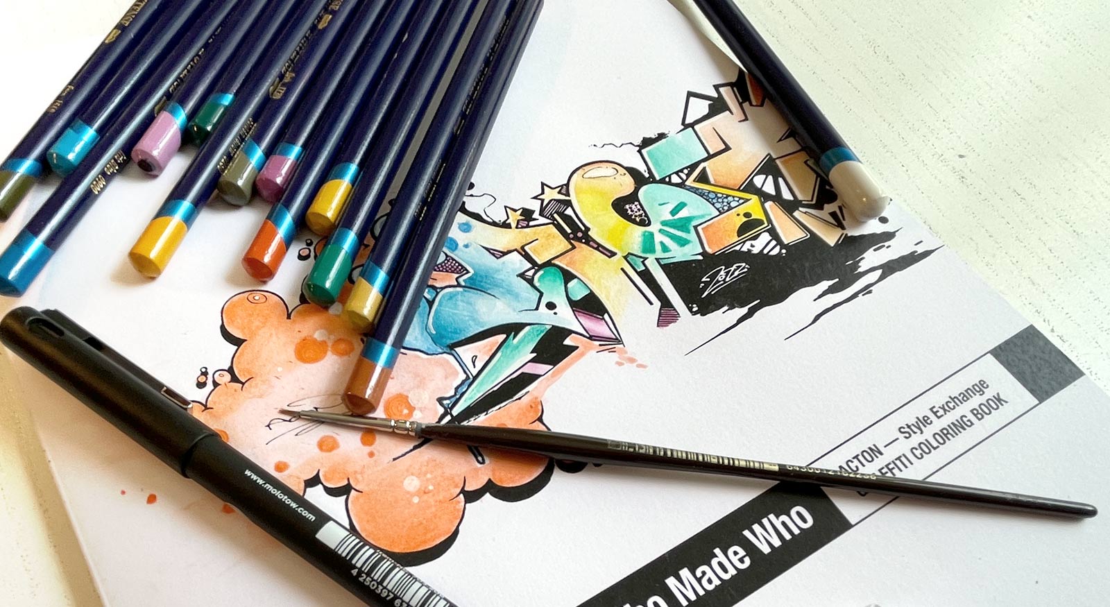 Graffiti coloring book with various crayons, marker and a fine brush on top of it.