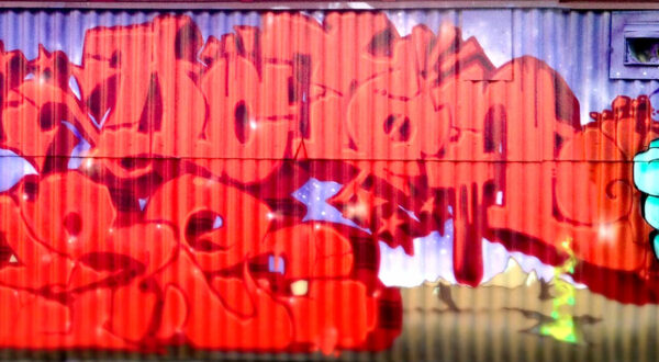 Red graffiti on rigged metal wall.