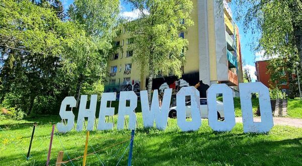 White wooden Sherwood-letters in front of an apartment building.